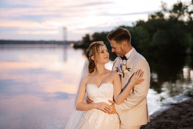 La sposa in un vestito gonfio bianco e lo sposo in t sulla riva del fiume