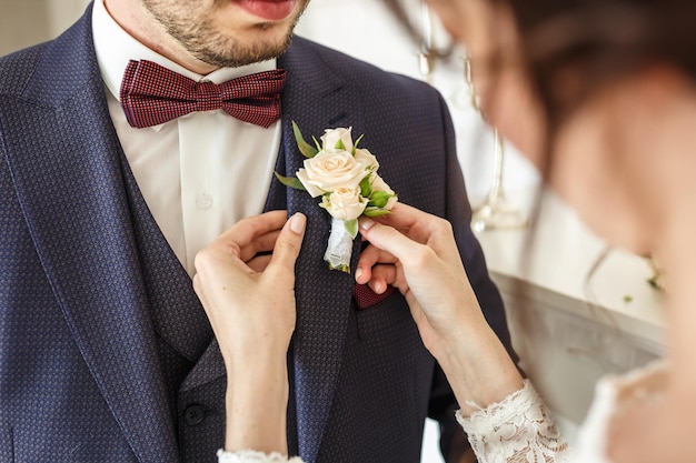 La sposa mette lo sposo sul fiore all'occhiello delle rose bianche il giorno del matrimonio