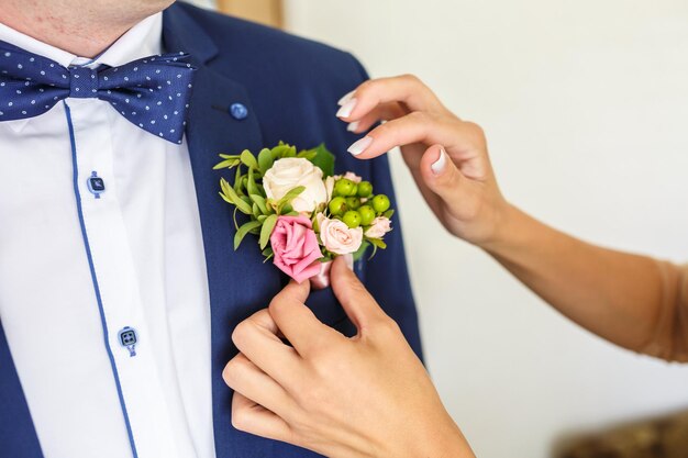 La sposa mette lo sposo sul fiore all'occhiello di rosa e rosa bianca il giorno del matrimonio