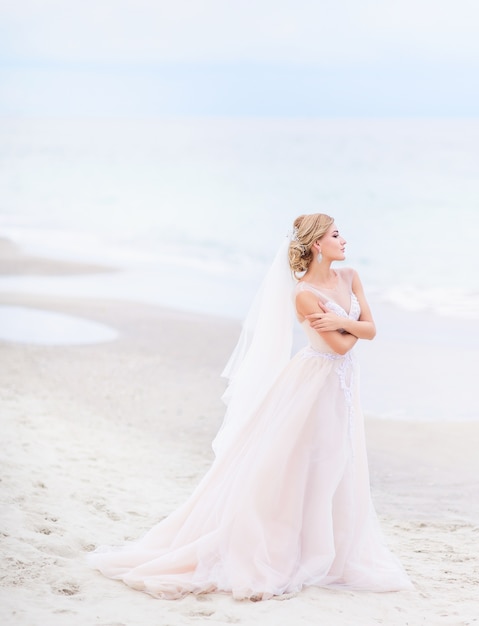 La sposa sembra in piedi splendida sulla sabbia bianca prima del mare