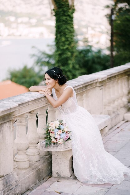 La sposa si siede su una panchina in un luogo panoramico nella città vecchia si appoggia alla ringhiera e sorride