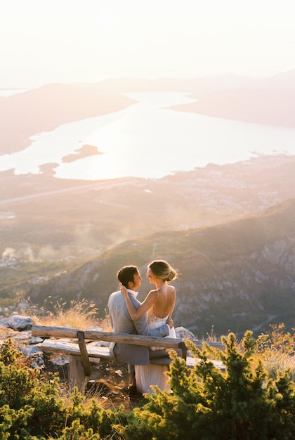 La sposa si siede sulle ginocchia dello sposo su una panchina in cima a una montagna