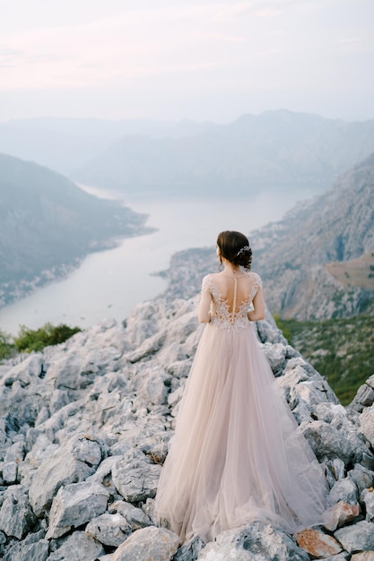 La sposa si trova su una montagna rocciosa sullo sfondo della vista posteriore della baia di Kotor