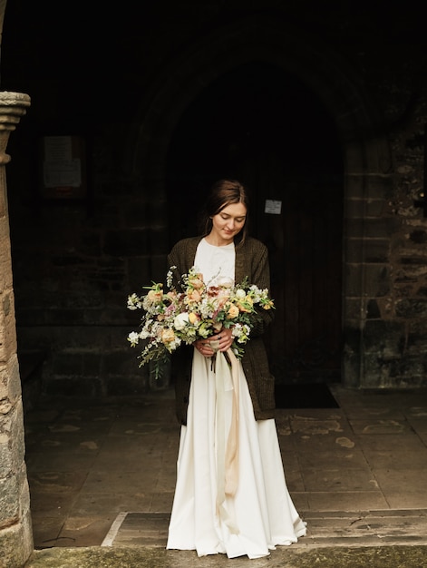 La sposa tiene il mazzo di nozze e guarda giù durante il giorno nuvoloso. primo piano, grande bel mazzo