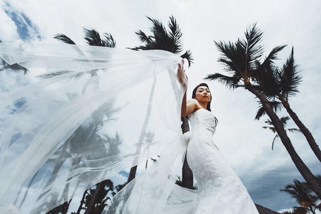 La sposa tiene il suo vestito in posa tra palme al vento