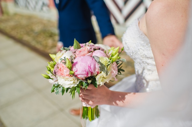 La sposa tiene in mano un bouquet da sposa di rose e peonie.