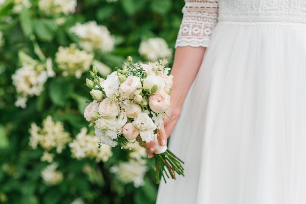 La sposa tiene tra le mani un bellissimo bouquet da sposa di fiori bianchi e di pesco