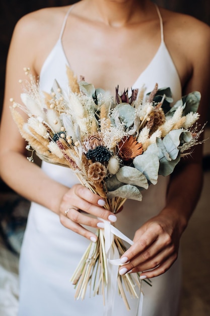 La sposa tiene tra le mani un bellissimo bouquet di fiori secchi in stile boho