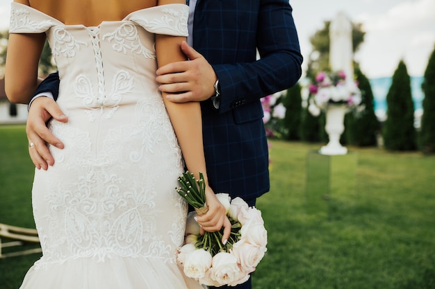 La sposa tiene un bellissimo bouquet e lo sposo la abbraccia per la schiena.