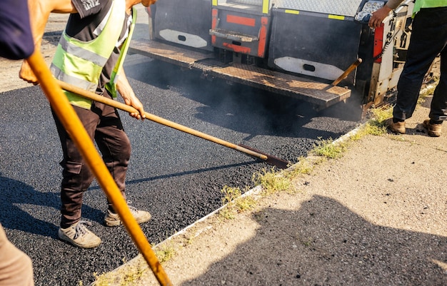 La squadra di costruzione di strade ha utilizzato le pale per spargere più asfalto sopra la nuova pavimentazione