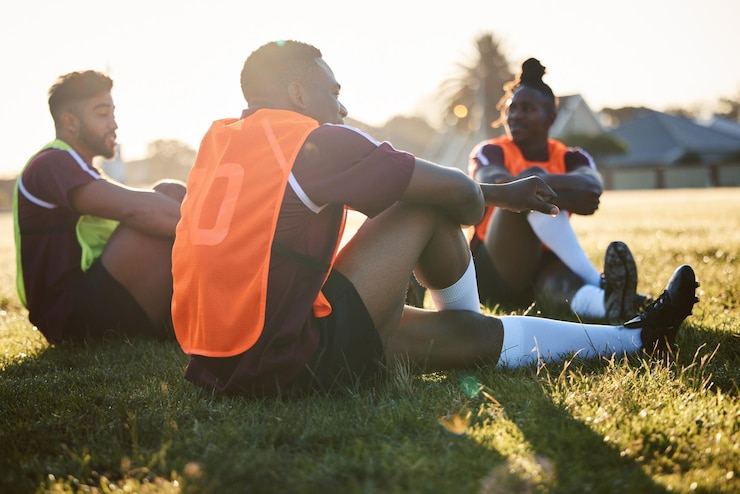 Foto la squadra di rugby e gli uomini si rilassano sul campo all'aperto parlando e comunicando all'alba del mattino gruppo di atleti sportivi e giocatori seduti sull'erba dopo l'allenamento fisico o l'allenamento degli amici nel gioco