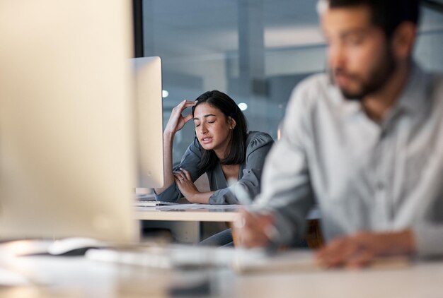 La stanchezza eccessiva porta a prestazioni insufficienti Inquadratura di una giovane donna che si sente stressata mentre usa le cuffie e il computer a tarda notte in un ufficio moderno