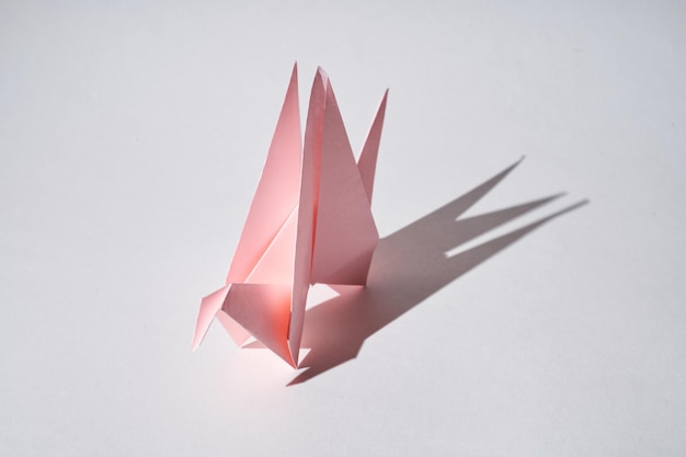 La statuetta del drago di carta rosa si trova su uno sfondo bianco in condizioni di luce intensa