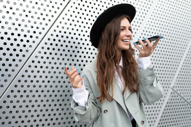 La stilista europea di una giovane donna con un cappello scrive un messaggio vocale al telefono