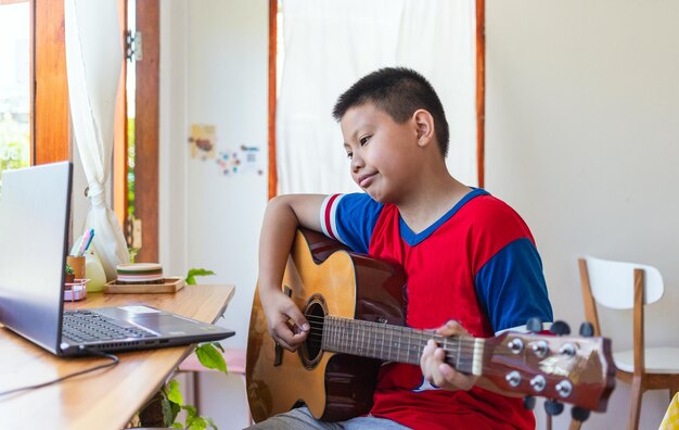 La storia di un ragazzo che guarda un computer portatile mentre si prepara ad esercitarsi a suonare la chitarra a casa