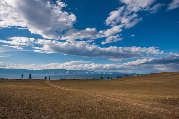 La strada attraverso la steppa verso il lago Baikal Nel cielo azzurro belle nuvole una corsia di montagne dietro il lago