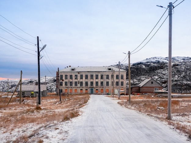 La strada per la costruzione di una vecchia scuola abbandonata sullo sfondo delle colline artiche in inverno.