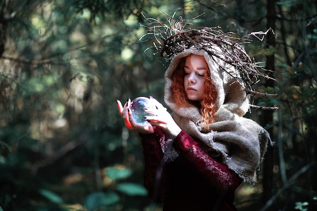 La strega dai capelli rossi tiene un rituale con una sfera di cristallo nella foresta
