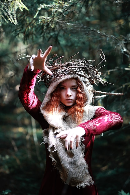 La strega dai capelli rossi tiene un rituale con una sfera di cristallo nella foresta