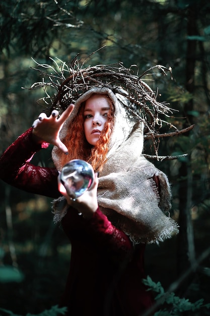 La strega dai capelli rossi tiene un rituale con una sfera di cristallo nella forestaxA