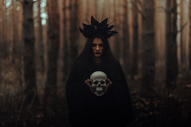 La strega terribile nera tiene il cranio di un uomo morto nelle sue mani in una foresta oscura