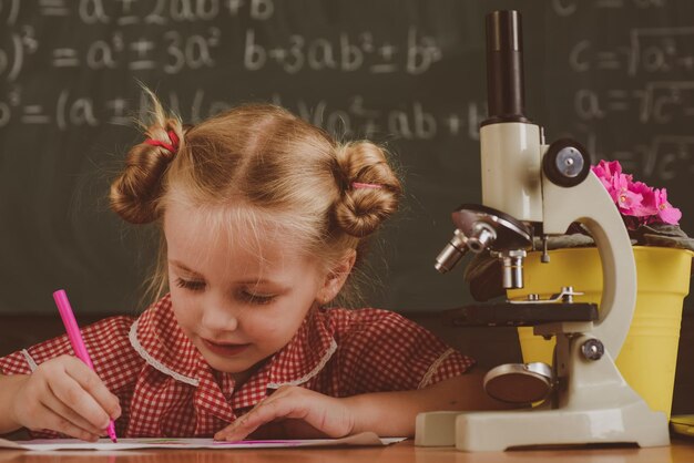 La studentessa lavora sulla ricerca biologica con il microscopio Bambina studia in classe di biologia a scuola filtro vintage