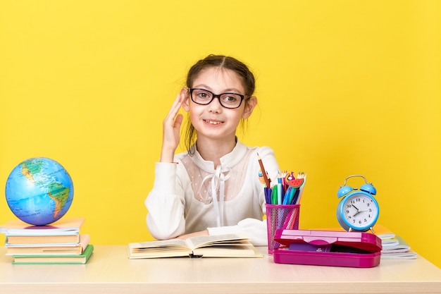 La studentessa si siede alla scrivania e alza la mano per avere una risposta. Di nuovo a scuola. Il nuovo anno scolastico. Concetto di educazione del bambino. Copia spazio