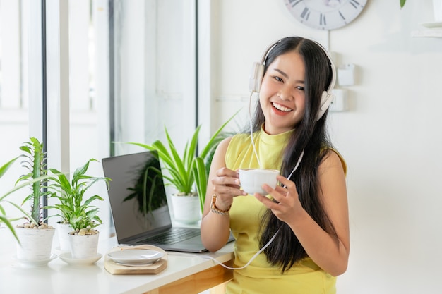 La studentessa sorridente asiatica indossa lo studio senza fili della cuffia online con l'insegnante di skype in una caffetteria,