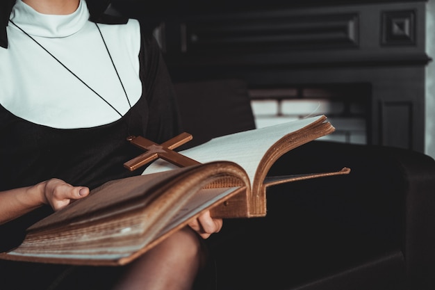 La suora in abito nero religioso tiene la Bibbia e posa sulla macchina fotografica con un grande libro su sfondo nero. Avvicinamento. concetto di religione.