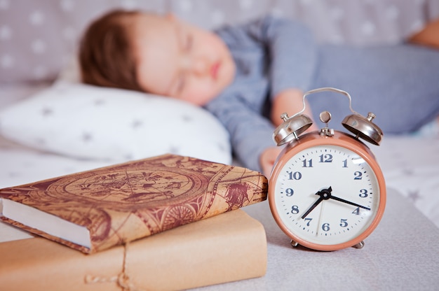 La sveglia si trova su uno scaffale con i libri, sullo sfondo il bambino dorme in un lettino