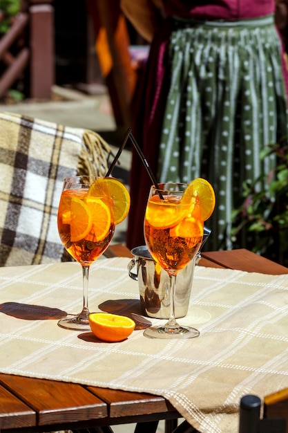 La tabella del plaid di vetro di cocktail dello spritz di Aperol lascia la luce solare arancione dell'ombra del secchiello del ghiaccio del sole