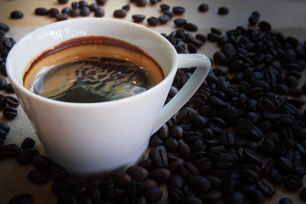 La tazza bianca di caffè espresso caldo con un gruppo di chicchi di caffè