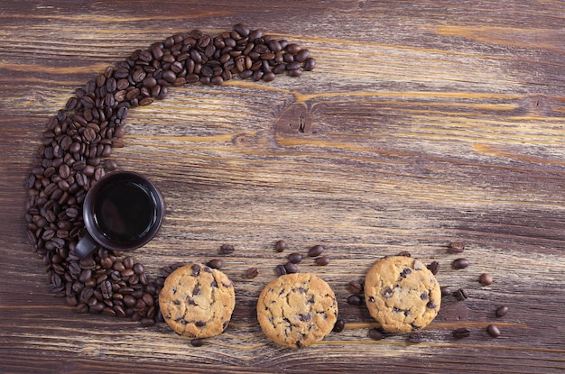 La tazza di caffè con biscotti al cioccolato e fagioli sparsi si trova su una vecchia superficie di legno, vista dall'alto con spazio per il testo