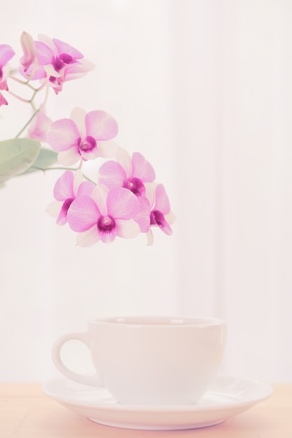 La tazza di caffè e la bella orchidea porpora fiorisce sulla tavola di legno