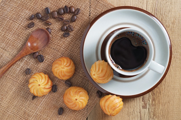 La tazza di caffè e la piccola crema pasticcera agglutina sulla tavola di legno, vista superiore