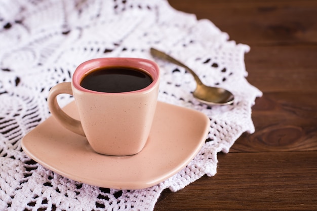 La tazza di caffè è sul tovagliolo traforato a maglia sul tavolo di legno