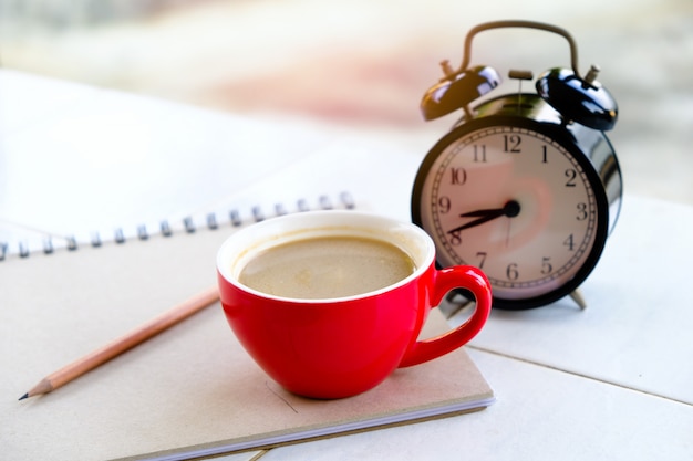 la tazza di caffè rossa è abbinata a un orologio nero, con libri e