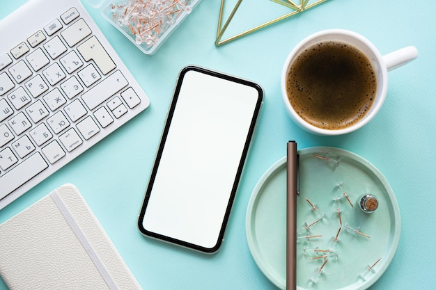 La tazza di caffè sul posto di lavoro blu pastello della signora freelance e il mockup dello smartphone sul tavolo