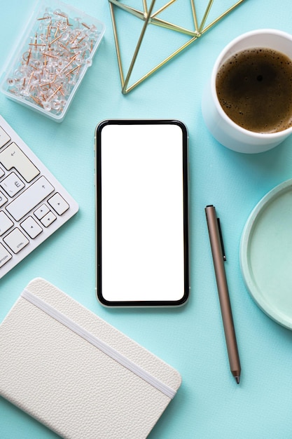 La tazza di caffè sul posto di lavoro blu pastello della signora freelance e il mockup dello smartphone sul tavolo