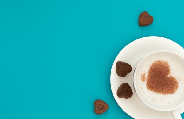 La tazza di cappuccino con cocao a forma di cuore su schiuma di caffè e cuori di cioccolato su sfondo blu