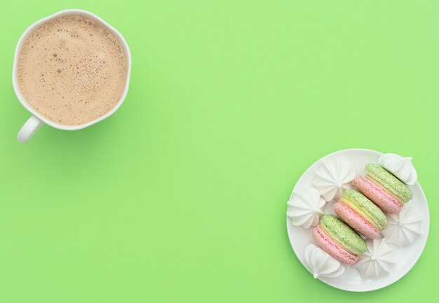 La tazza di cappuccino e deliziosi macarons con merengues bianco. Stile piatto