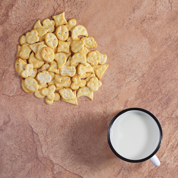 La tazza di latte con cracker di diverse forme si trova su uno sfondo di pietra marrone, vista dall'alto