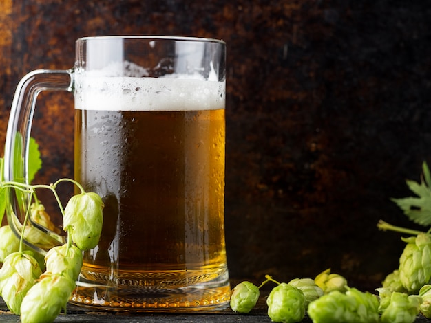 La tazza di luce ha saltato la birra su un fondo arrugginito scuro con il luppolo verde