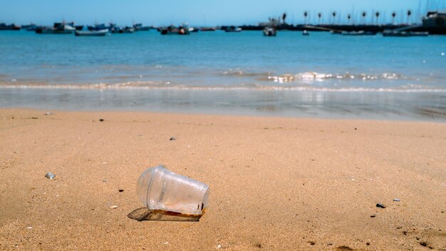 La tazza di plastica della spazzatura lasciata sulla spiaggia fa inquinamento