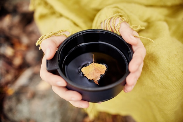 La tazza di tè caldo in mano della donna è l'autunno in una foresta