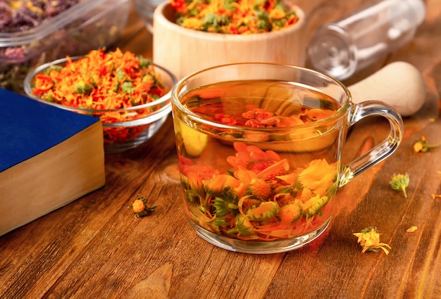 La tazza di tè dalla calendula secca fiorisce su una tavola di legno. Raccolta di erbe.