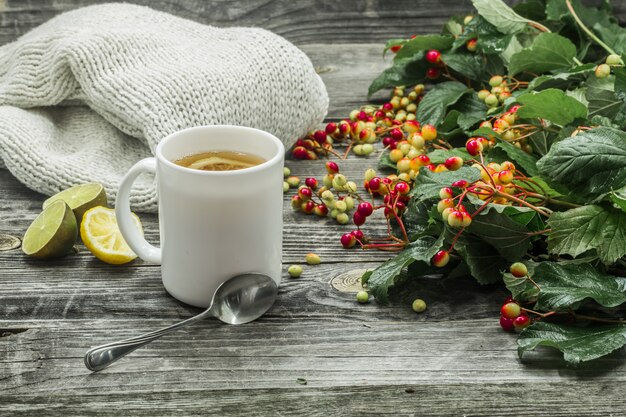 la tazza di tè su un bellissimo sfondo in legno con maglione invernale, bacche, autunno