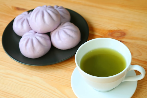 La tazza di tè verde con il mucchio confuso della patata dolce porpora ha cotto a vapore i panini sulla tavola di legno