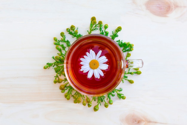 La tazza di tisana nera con rami, fiori di camomilla farmacia sulla tavola di legno