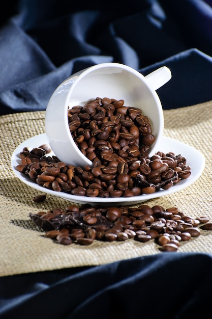 La tazza rovesciata con chicchi di caffè sul supporto della cucina per tessuto caldo e blu